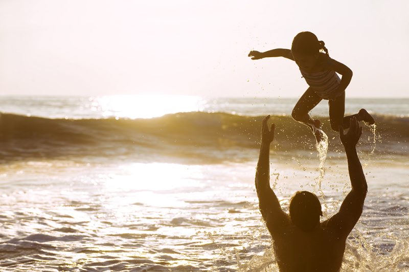 Father Playing and Throwing Daughter Up in Ocean at Sunset