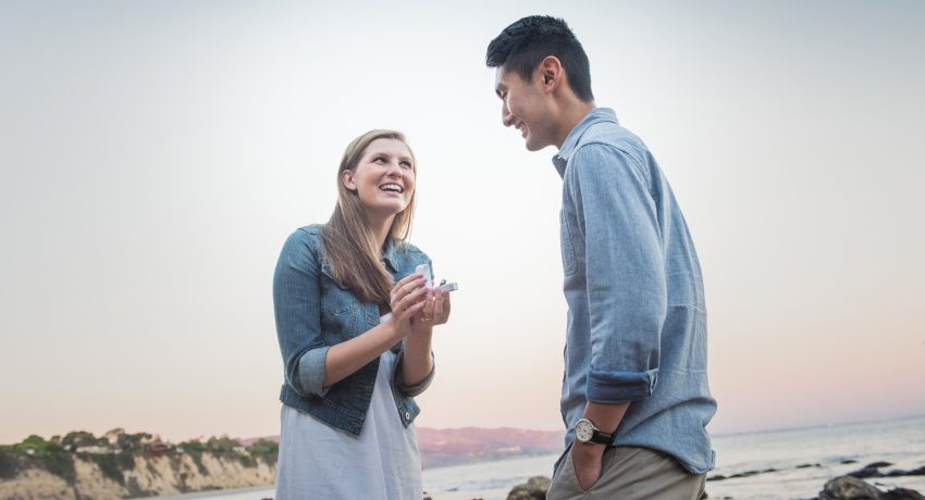 A true role reversal. Caucasian young woman proposing  with a diamond ring to his Japanese boyfriend at the beach during sunset.